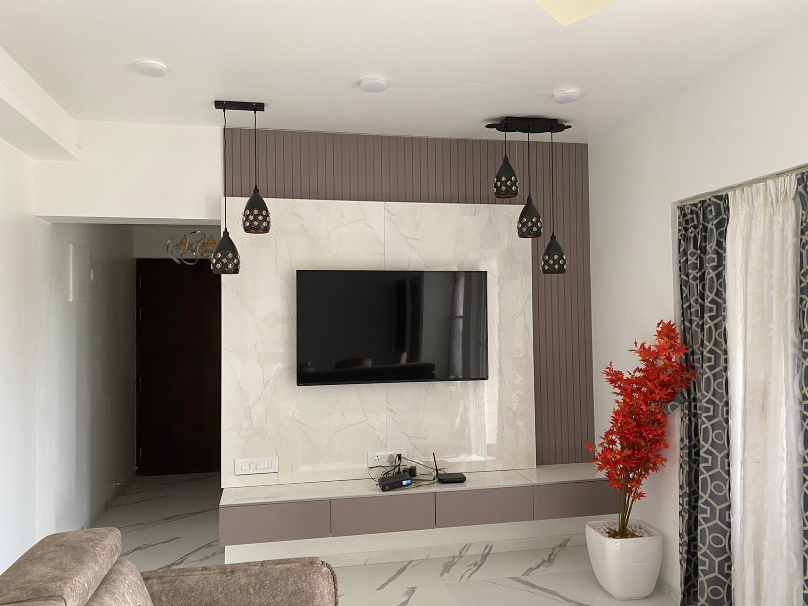 TV wall with a marble-look panel, wooden slats and pendant lights